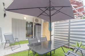 Um pátio com mesa e cadeiras de vidro, guarda-sol e cerca de madeira.