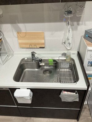 A kitchen with a stainless steel sink, a wooden cutting board, and a dish rack.