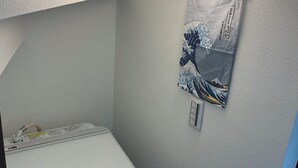 Un lavadero pequeño y funcional con lavadora de carga frontal, tendedero de pared y una ventana.