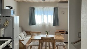 Un espacio habitable compacto con kitchenette, una zona de comedor con mesa y sillas, un sofá y una ventana con cortinas.