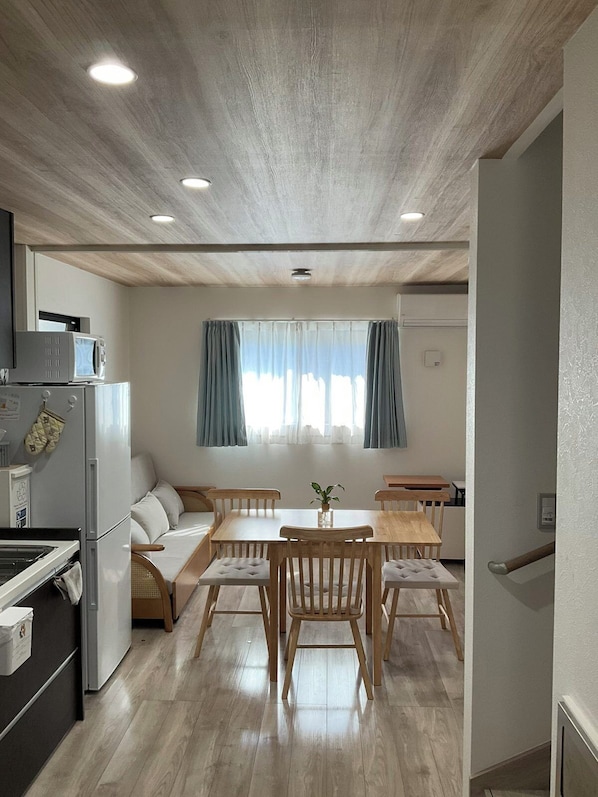 A compact living space with a kitchenette, a dining area with a table and chairs, a sofa, and a window with curtains.