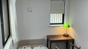 Una habitación pequeña y luminosa con una cama, un escritorio, una silla y una ventana con cortinas.