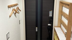 Una habitación pequeña con una puerta oscura, un perchero de madera, un escritorio de madera y suelo de baldosas.