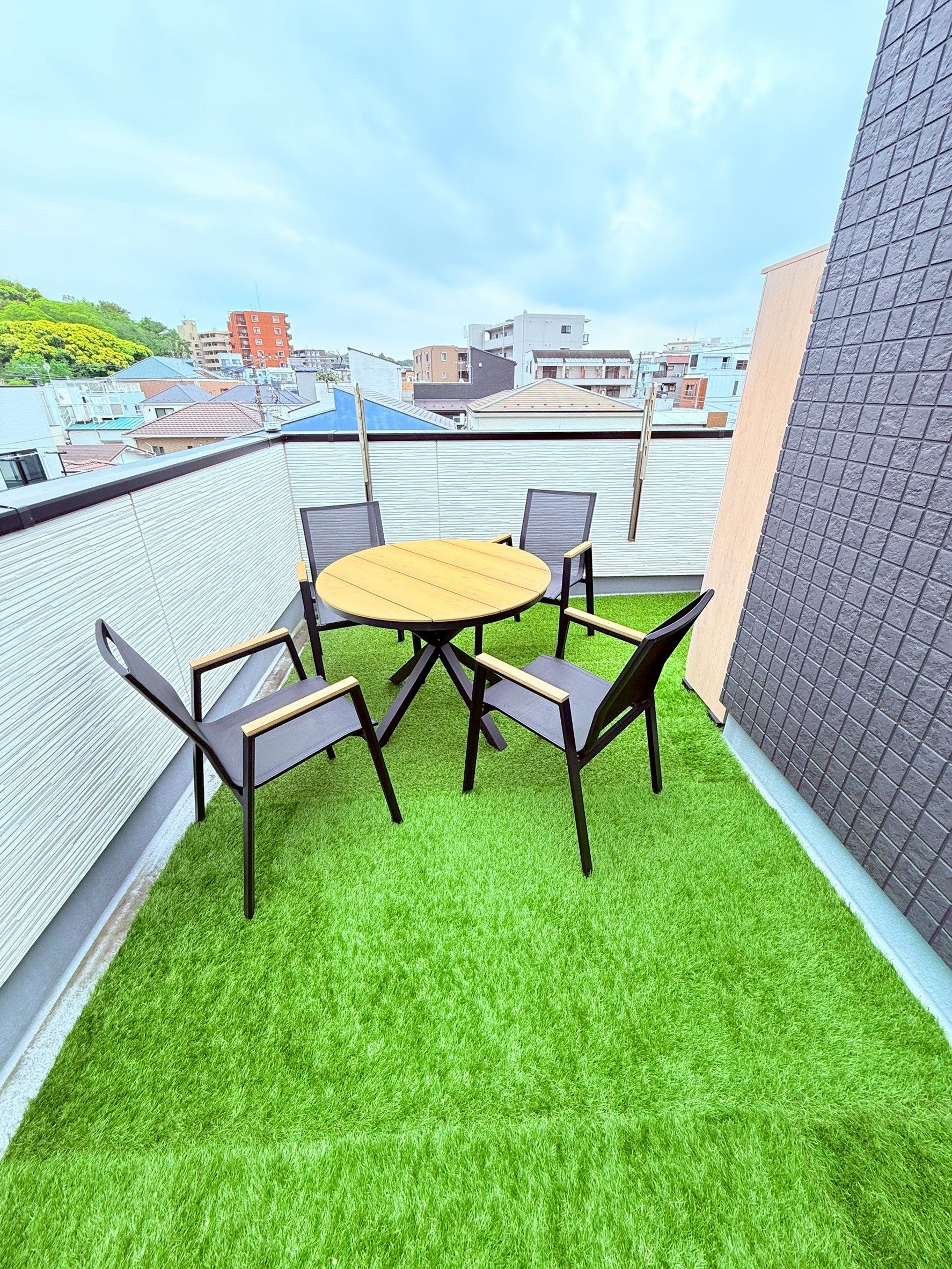 A rooftop terrace with a round table and four chairs, surrounded by artificial green grass.