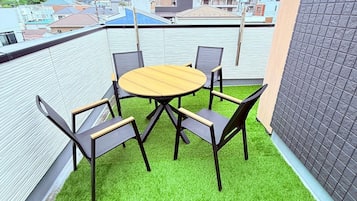 A rooftop terrace with a round table and four chairs, surrounded by artificial green grass.