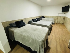Una habitación con dos camas, cada una con una colcha blanca y varias almohadas. Un televisor está montado en la pared, y hay una pequeña mesa apoyada contra la pared.
