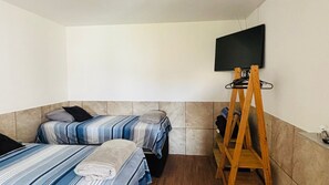 Una habitación pequeña y limpia con dos camas, un televisor montado en la pared y un atril de madera.