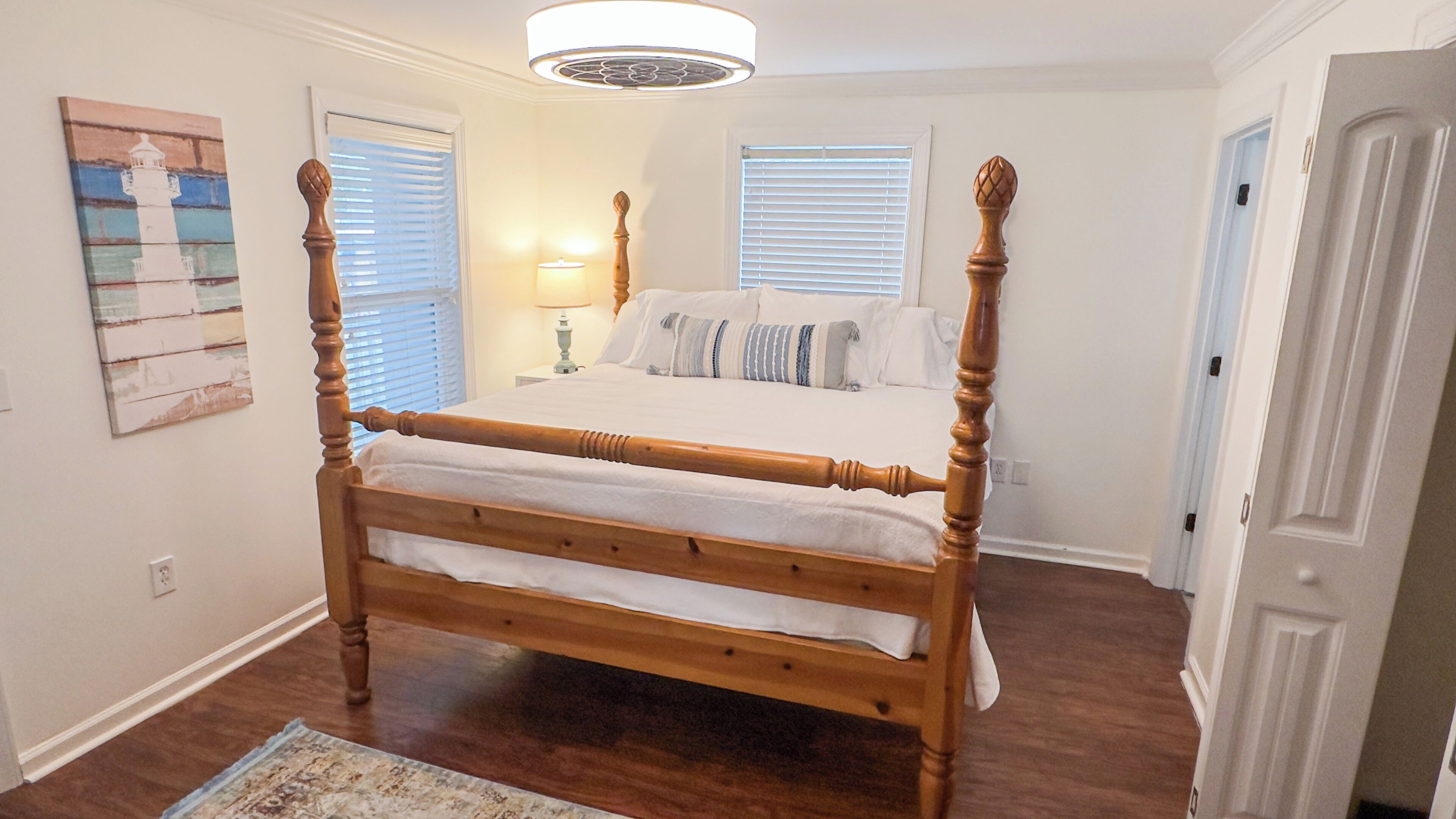 Een hemelbed met houten frame, witte beddengoed en een nachtkastje met een lamp.