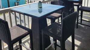 Ein Balkon mit Korbmöbeln und einem Glastisch, der auf eine Straße mit parkenden Autos und Gebäuden blickt.