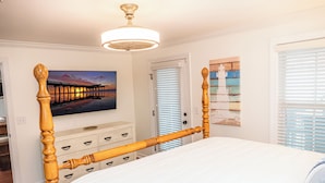 Ein Schlafzimmer mit einem hölzernen Himmelbett, einem Deckenventilator, einem Bild von einem Pier und einer Tür mit Jalousien.