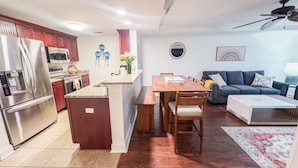Eine moderne Küche mit einer zentralen Kochinsel, einem Essbereich mit Holztisch und -stühlen, einer Couch und einem Deckenventilator.