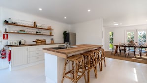 A modern kitchen with white cabinetry, a wooden island with stools, and a dining area with a table and chairs.