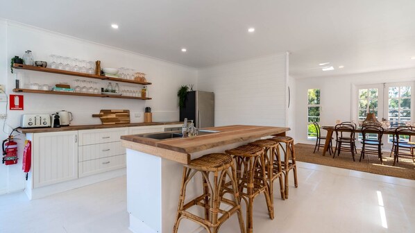 A modern kitchen with white cabinetry, a wooden island with stools, and a dining area with a table and chairs.