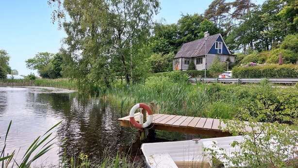 A house by a calm river with a dock and a lifebuoy.