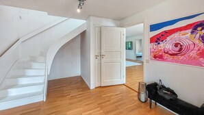 A modern interior with a wooden floor, a white staircase, a door leading to another room, and a colorful abstract painting on the wall.