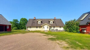 A two-story house with a gravel driveway, a front lawn, and a red barn to the left.