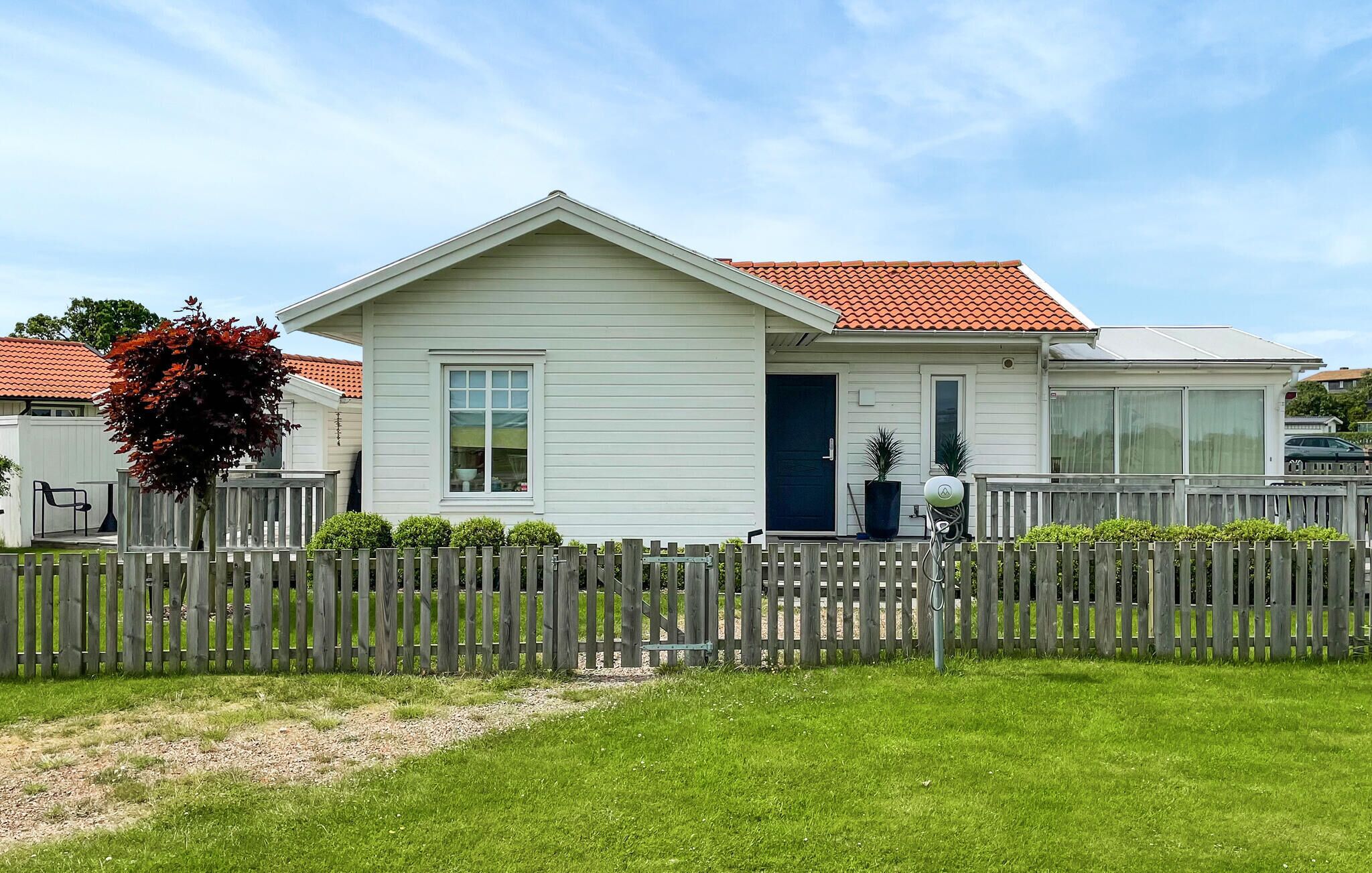 Ett envåningshus med ett rött tegeltak, vit träpanel och ett lågt, vitt staket.