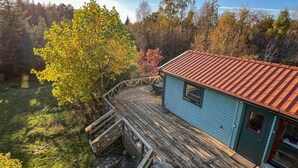 A wooden deck leading to a small cabin with a red-tiled roof, surrounded by autumn foliage. - Awesome home in Sturkö with sauna (Sturkö)