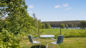A table and two chairs in a grassy area with a view of a lake and forest.
