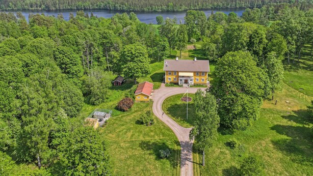 A large yellow house with a red roof surrounded by lush greenery and a lake in the background. - Nice apartment in Mullsjö with sauna (Mullsjö)