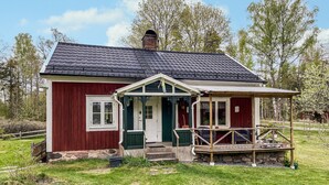 A small, single-story house with a red exterior and a white door, featuring a porch with a wooden railing and a small table. - 2 bedroom awesome home in Gislatorp (Gislatorp)