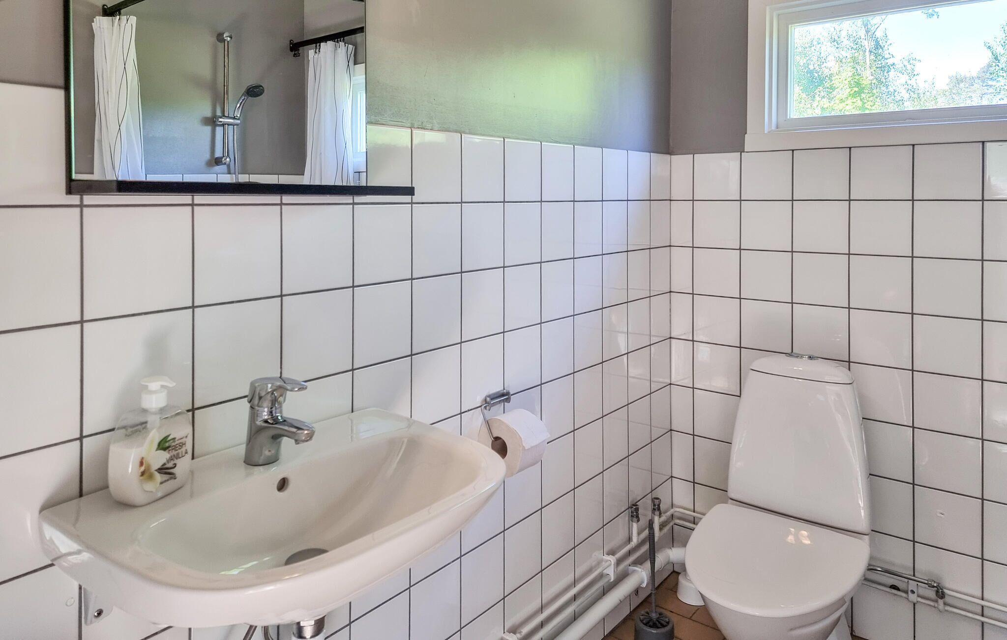 A bathroom with white tiles, a sink, a toilet, and a window.