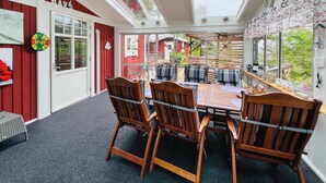 A cozy room with a wooden table and chairs, a large window with a view of a red building, and a ceiling fan.