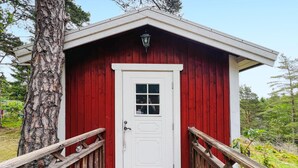 A red wooden cabin with a white door, a small window, and a porch with wooden railings.