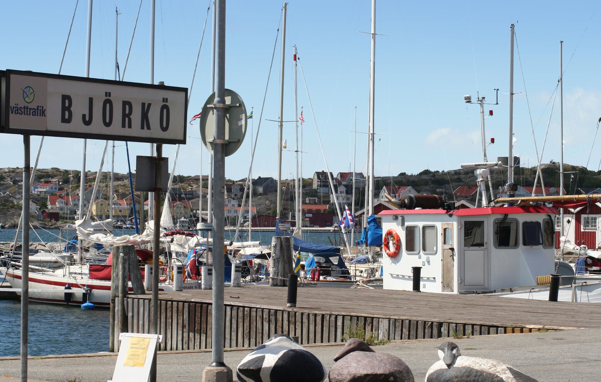 En hamn med båtar, en skylt med texten ”BJÖRKÖ” och en liten byggnad med ett rött tak.