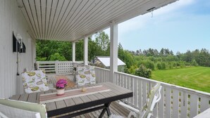 A covered porch with a wooden table and chairs, a potted plant, and a view of a green field. - Amazing home in Kristinehamn with WiFi (Kristinehamn)