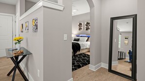 A modern interior with a glass table, a bed with a black and white patterned rug, and a hallway leading to a dining area. - Studio/Self Check-In/30+Day Stays (Goose Creek)