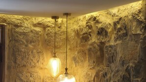 A room with a stone wall, a green upholstered bed, a small table with a vase, and a hanging light fixture. - A century of stories, now yours to experience. (Ehden)