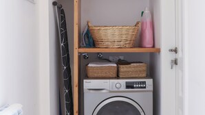 A laundry area with a washing machine, two wicker baskets on shelves, a radiator, and a door. - A century of stories, now yours to experience. (Ehden)