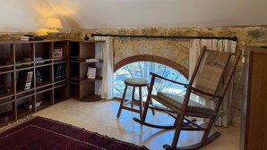 A cozy reading nook with a wooden rocking chair, a bookshelf, and a window with a view. - A century of stories, now yours to experience. (Ehden)