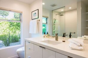 A modern bathroom with a large window, a sink, a mirror, and a shower.