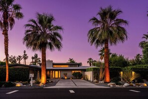 A modern house with a driveway, palm trees, and a purple sky. - Trousdale Palms: Luxe Mid-Century Pool Retreat (Palm Springs)