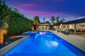 A modern pool area with a clear view of the pool, lounge chairs, and a building with large windows.