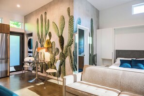 A modern living room with a large cactus wall, a sofa, a dining area with chairs, and a kitchen with a refrigerator.