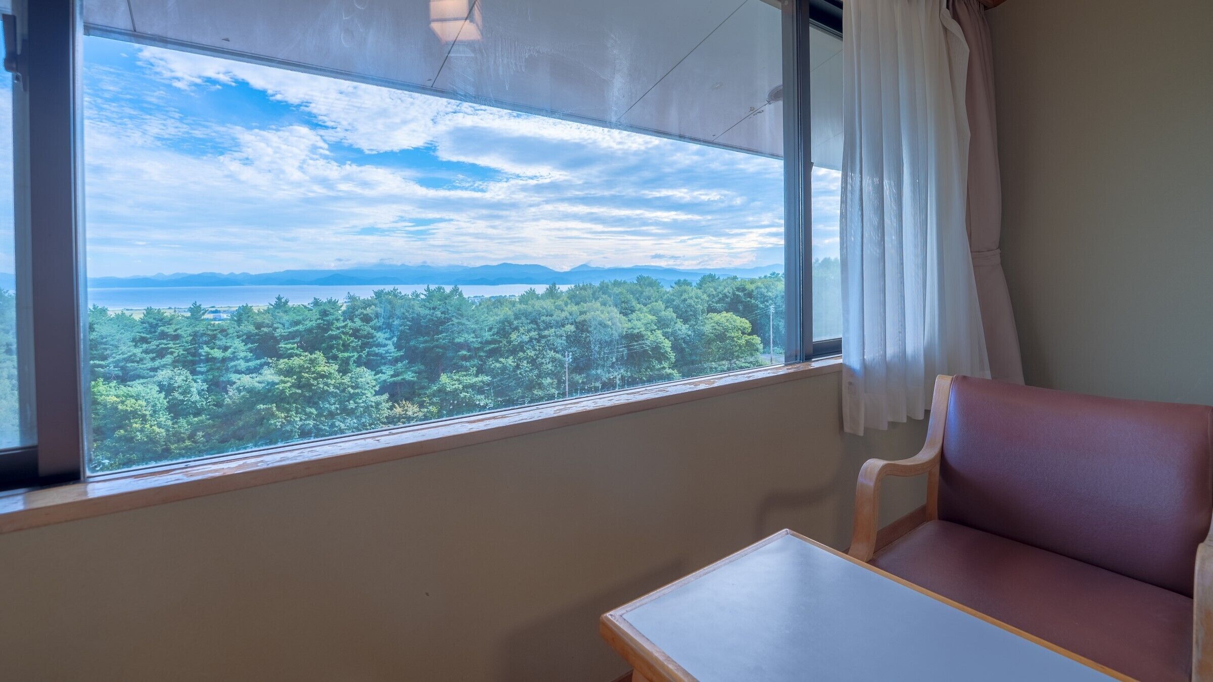A room with a large window offering a view of a forest and distant mountains.