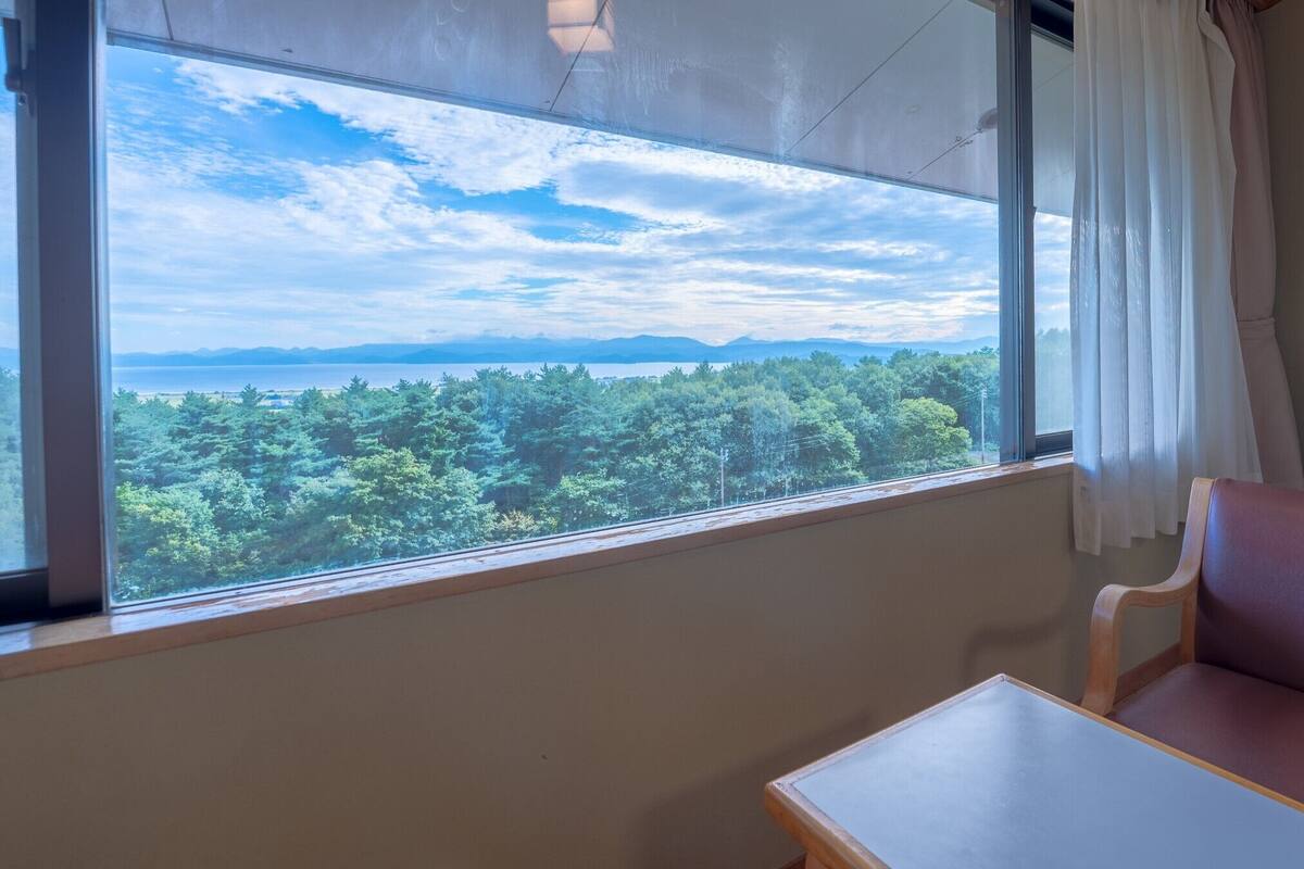A room with a large window offering a view of a forest and distant mountains.