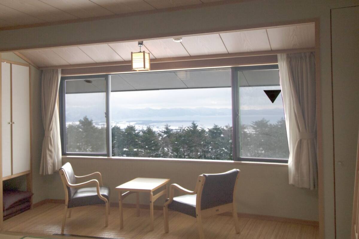 A room with a large window, two chairs, a small table, and a wooden floor.