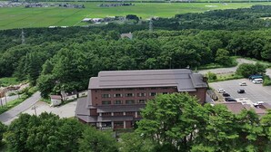A large building with a parking lot and a view of a lake and fields. - Inawashiro Kanko Hotel  (Inawashiro)