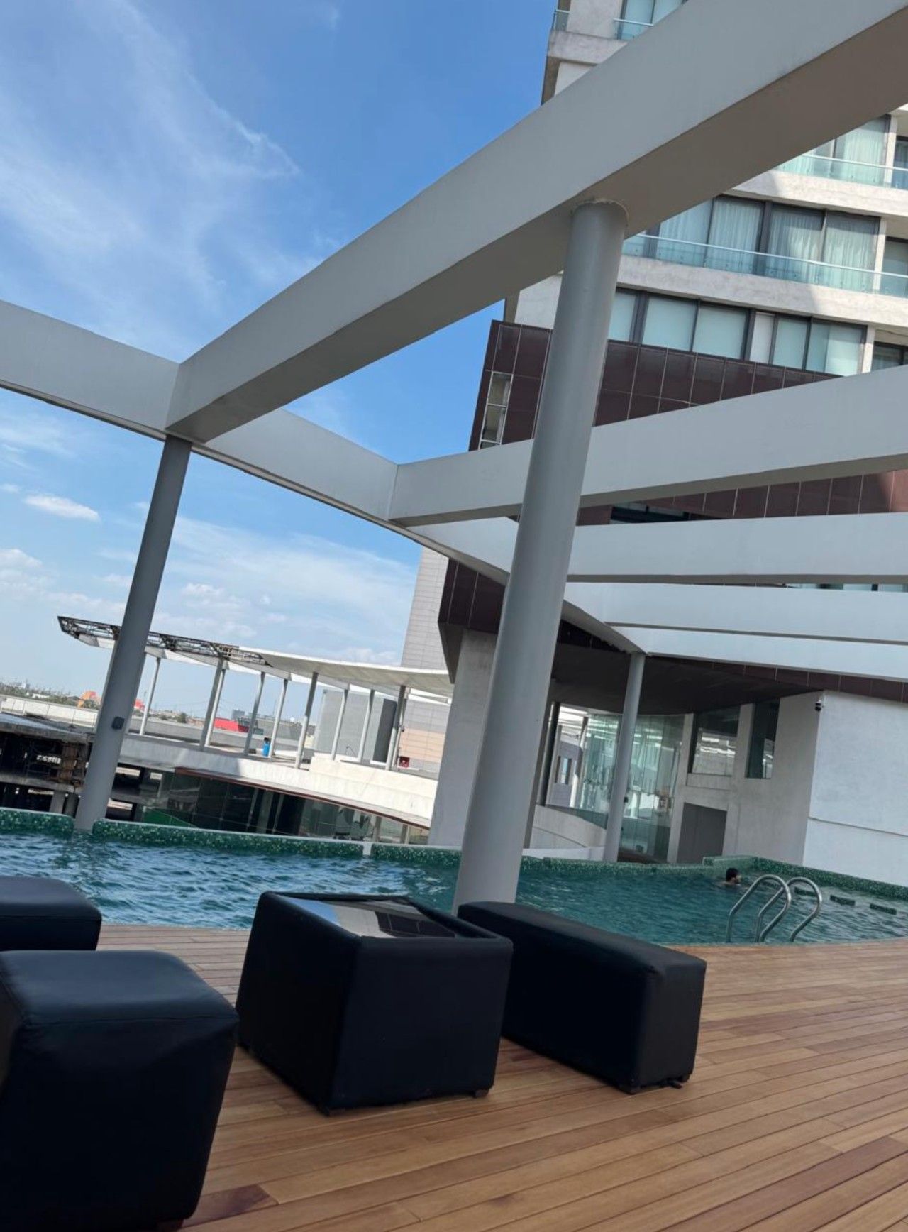 A deck with a pool, lounge chairs, and a modern building with glass windows in the background.
