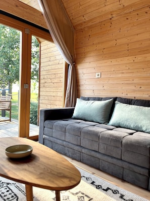 A cozy room with a grey sofa, a wooden table, and a large window with curtains.