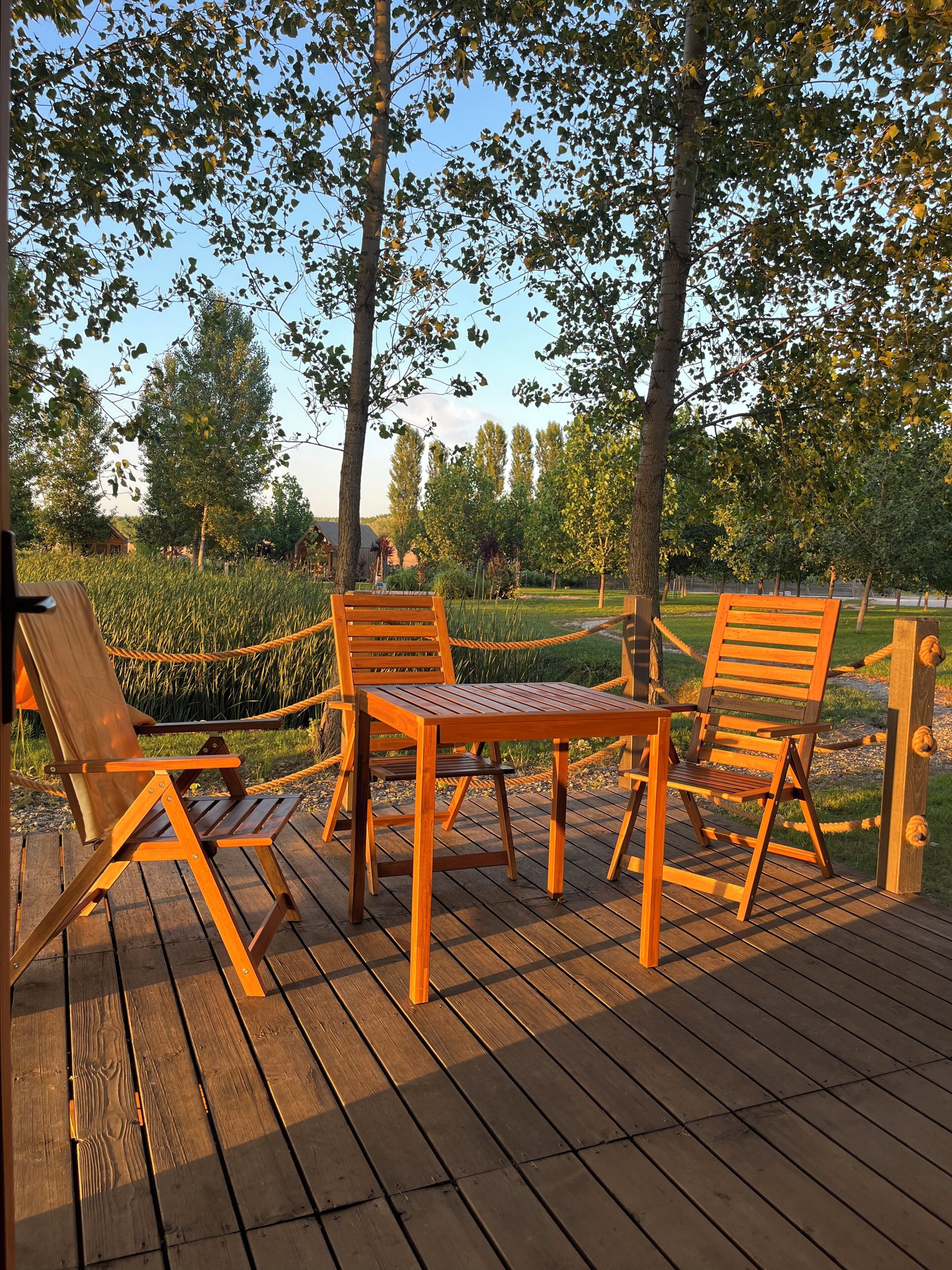 Une terrasse en bois avec une table et quatre chaises, entourée d’arbres et de verdure.