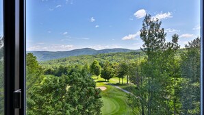 A view of a golf course with a forested landscape and distant mountains.