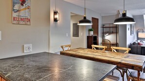 A dining area with a large table, two pendant lights, and a poster on the wall.