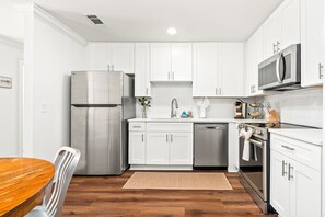 Una cocina moderna con armarios blancos, electrodomésticos de acero inoxidable y una mesa de comedor de madera.