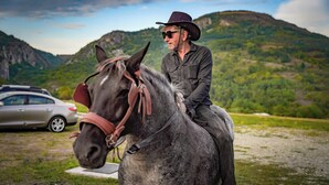 Une personne à cheval dans un paysage rural, avec des montagnes en arrière-plan.