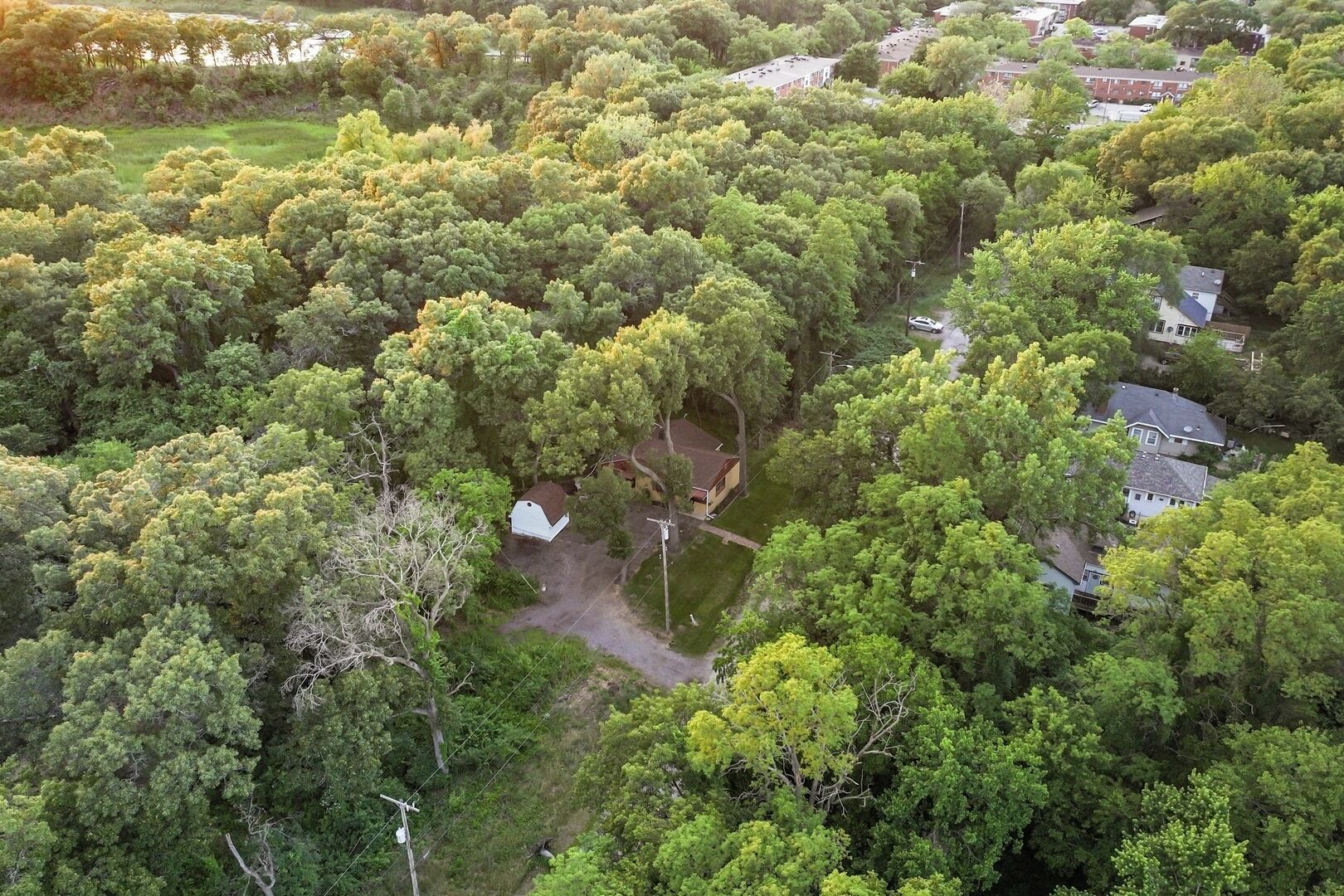An aerial view of a residential area with dense greenery, houses, and a small white building.